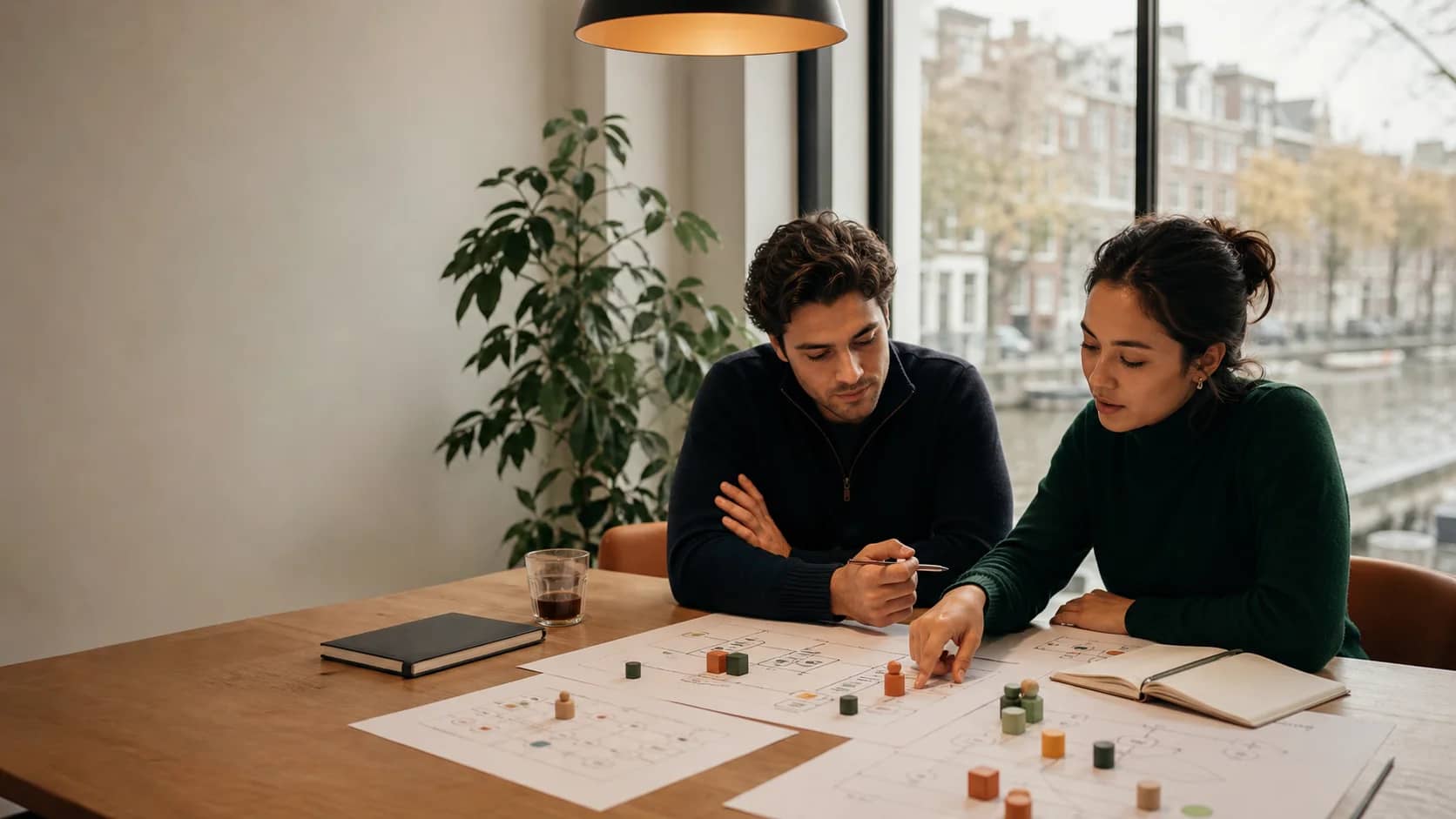 Two people compare documents and colored planning blocks beside an Amsterdam canal